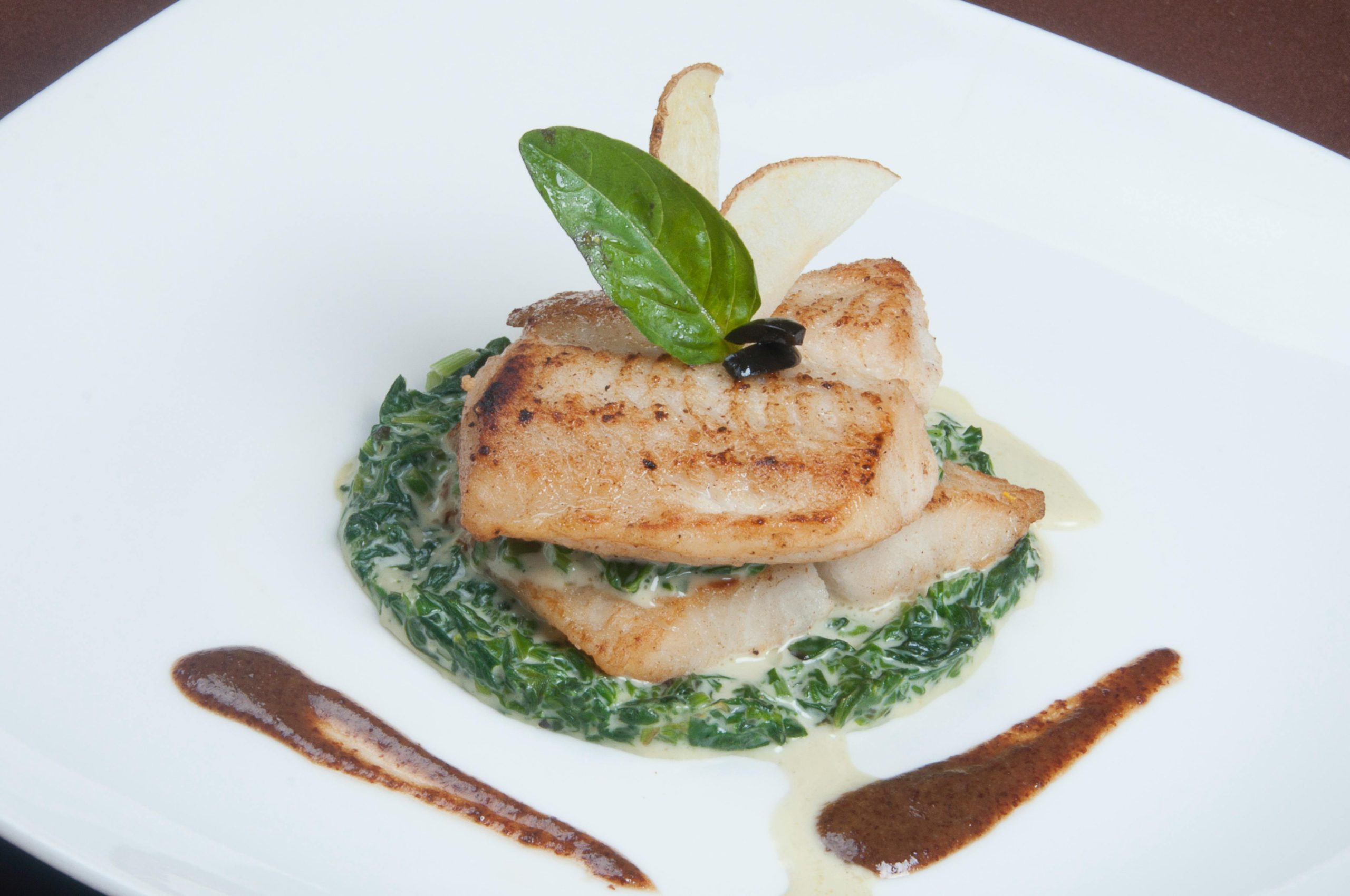 Elegant fish fillet dish with creamy spinach and gourmet presentation on white plate.